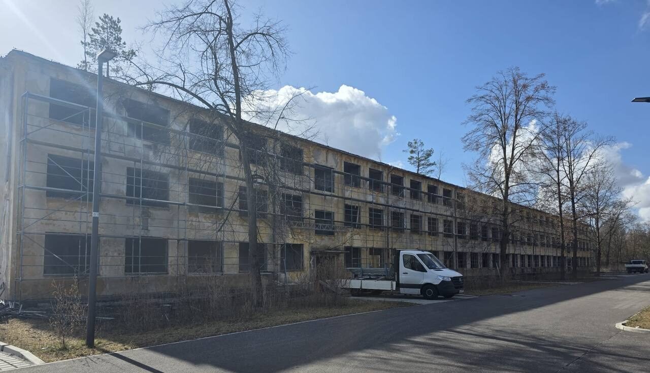 Mehrstöckiges Gebäude mit Gerüst an der Fassade, geparktem Transporter und Straße im Vordergrund